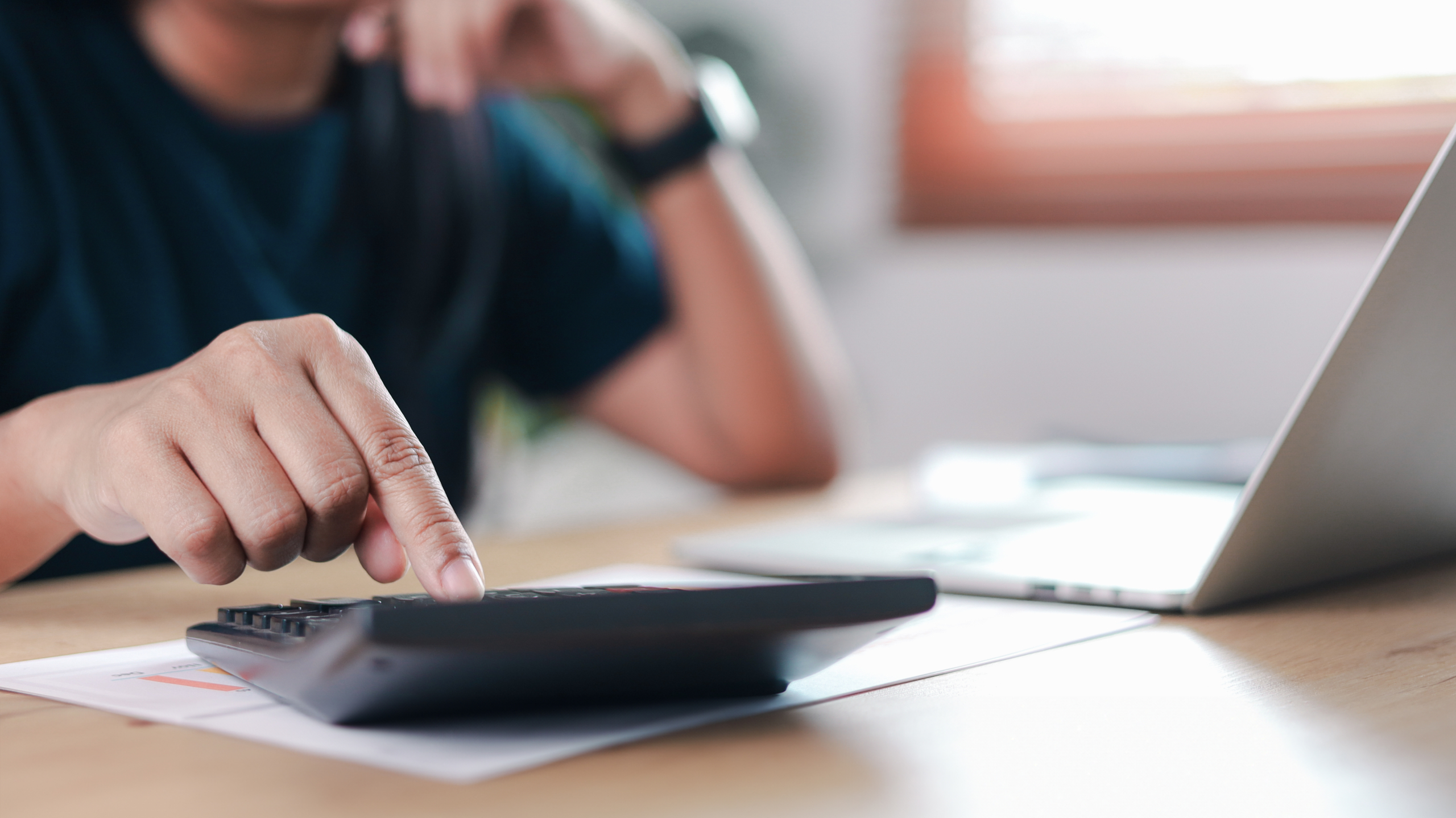 Business finance professional calculating budget using calculator and laptop on office desk. Concept of accounting, financial analysis, tax planning, corporate work, investment management,
